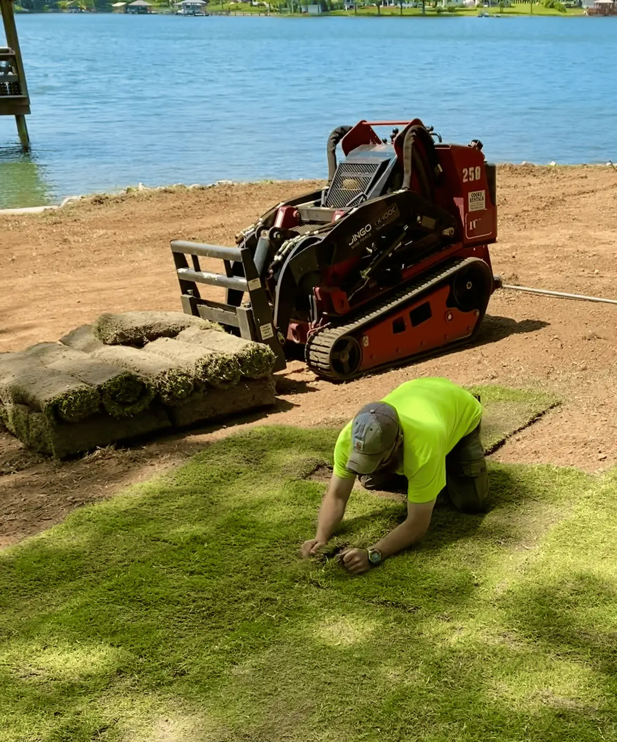 New sod going down by the lake, with a compact loader and a pallet of sod behind